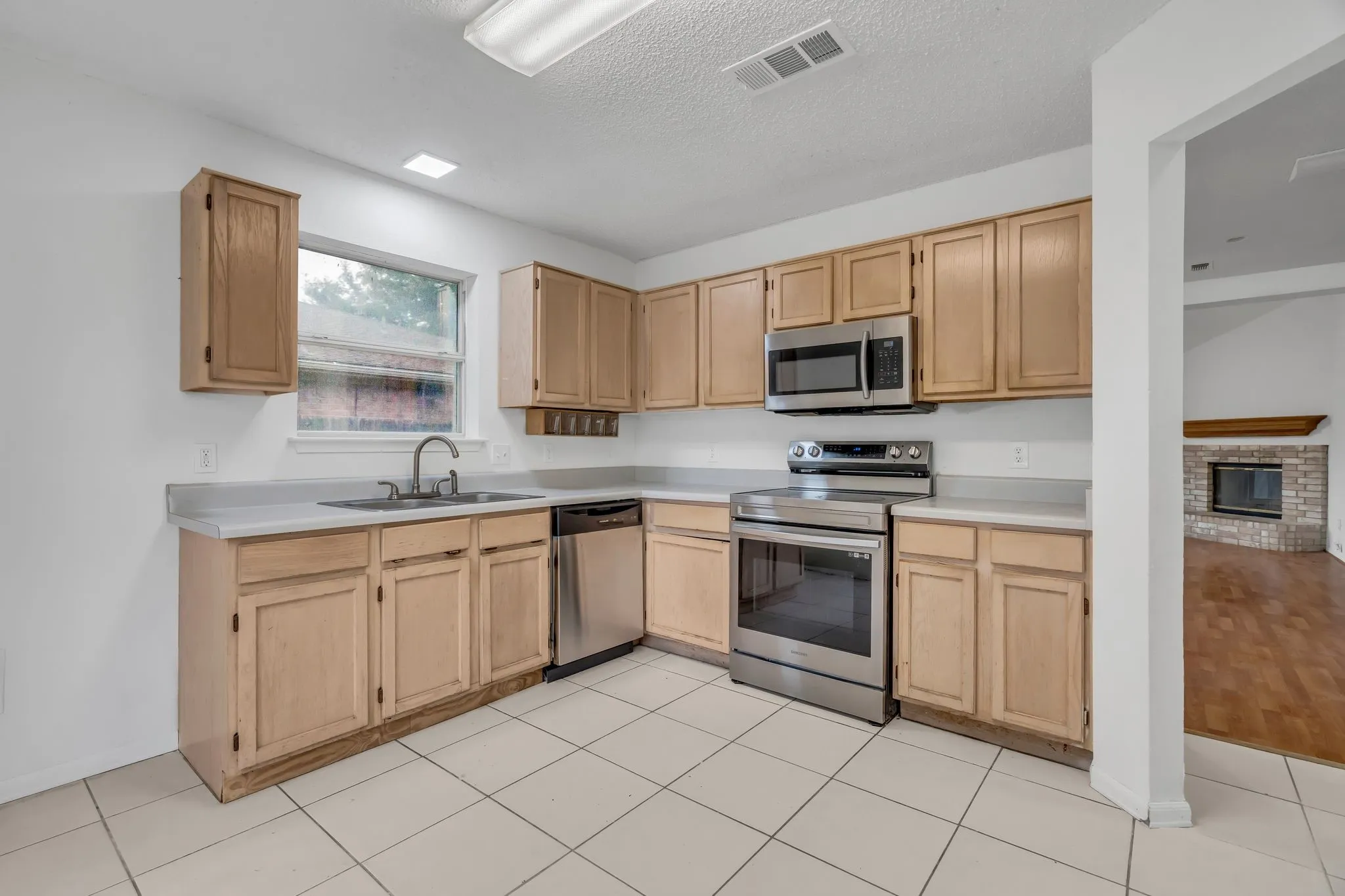 Kitchen with light brown cabinets, appliances with stainless steel finishes, light countertops, a textured ceiling, and light tile patterned flooring