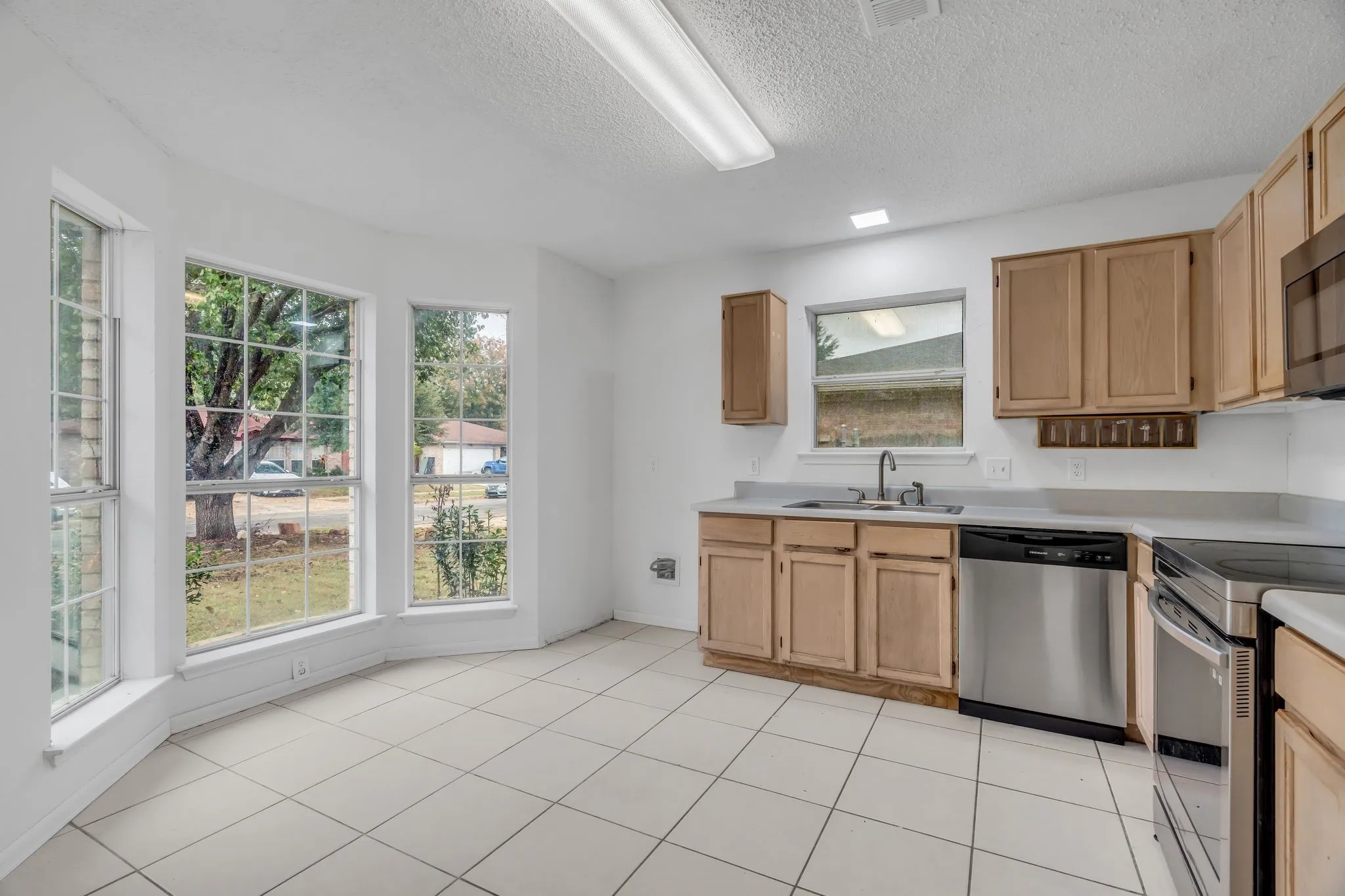 Kitchen featuring appliances with stainless steel finishes, light brown cabinetry, light countertops, a textured ceiling, and light tile patterned floors