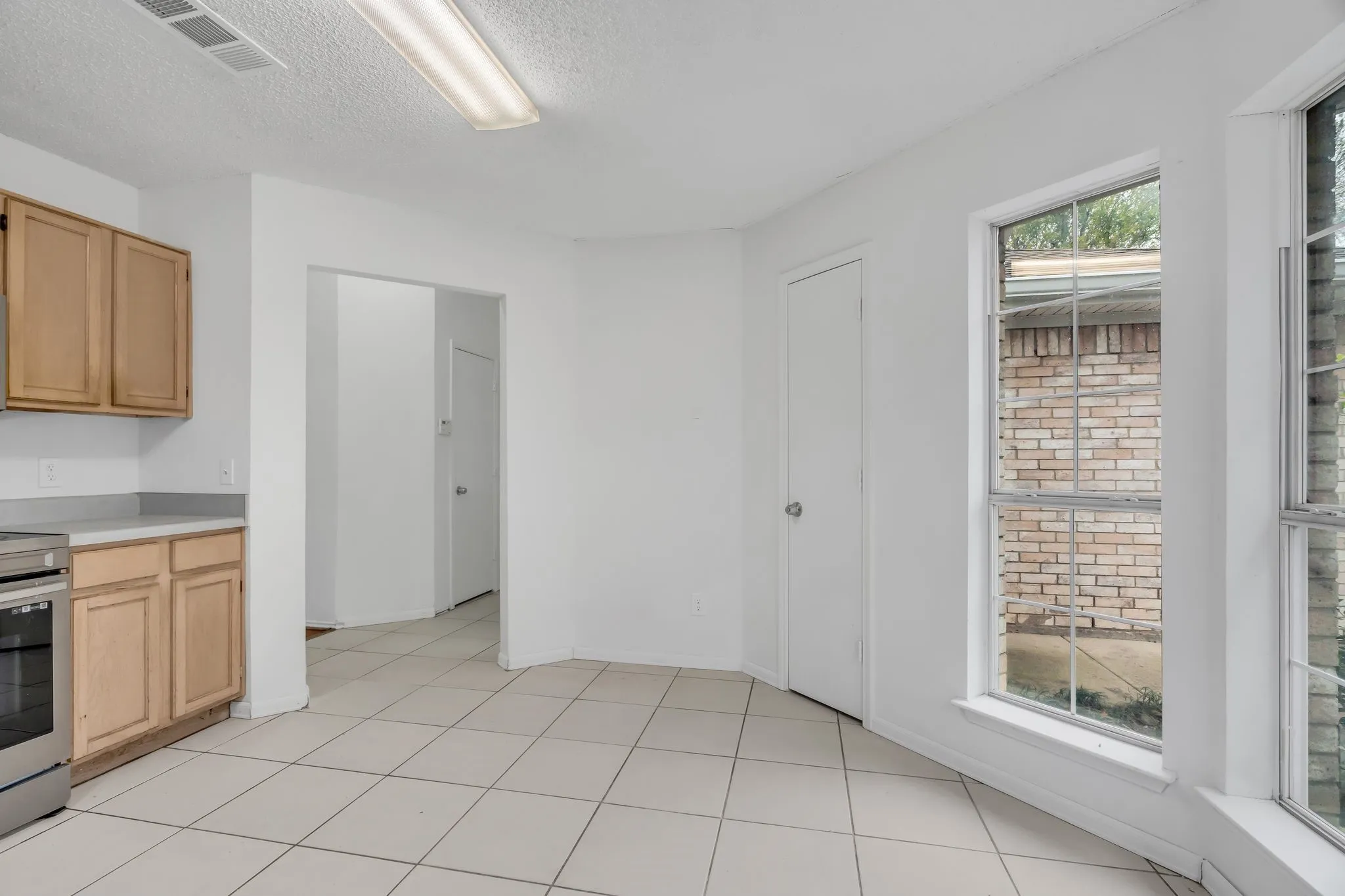 Kitchen featuring light brown cabinets, light countertops, stainless steel stove, a textured ceiling, and light tile patterned flooring