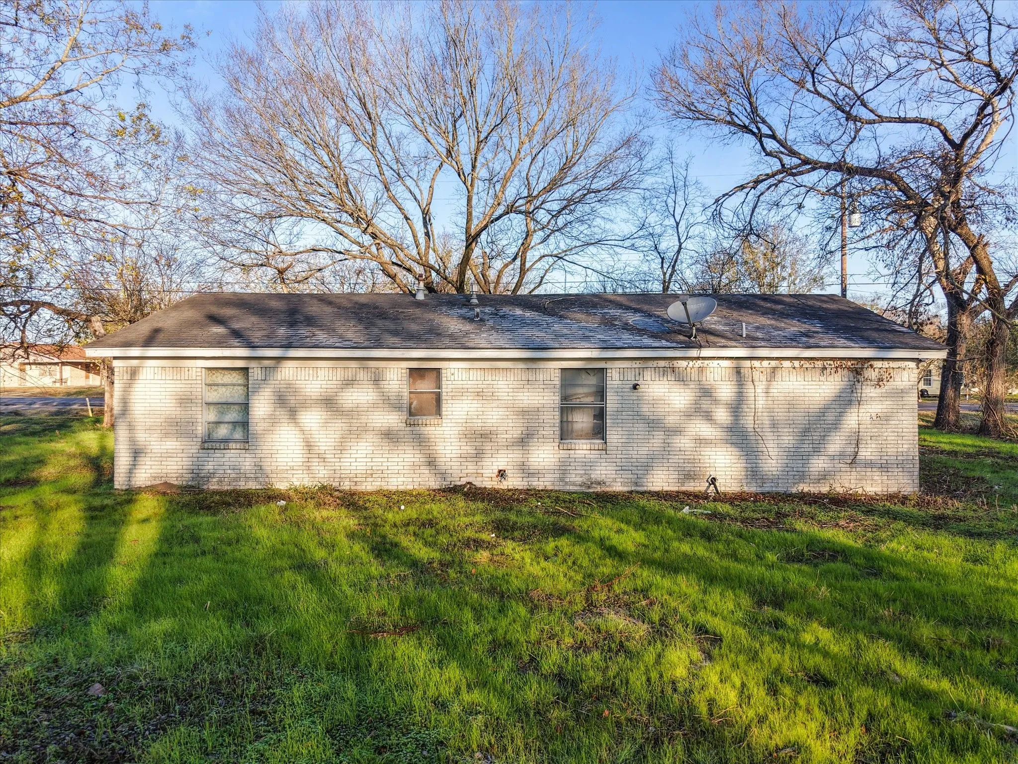 View of side of home with brick siding, a lawn, and roof with shingles