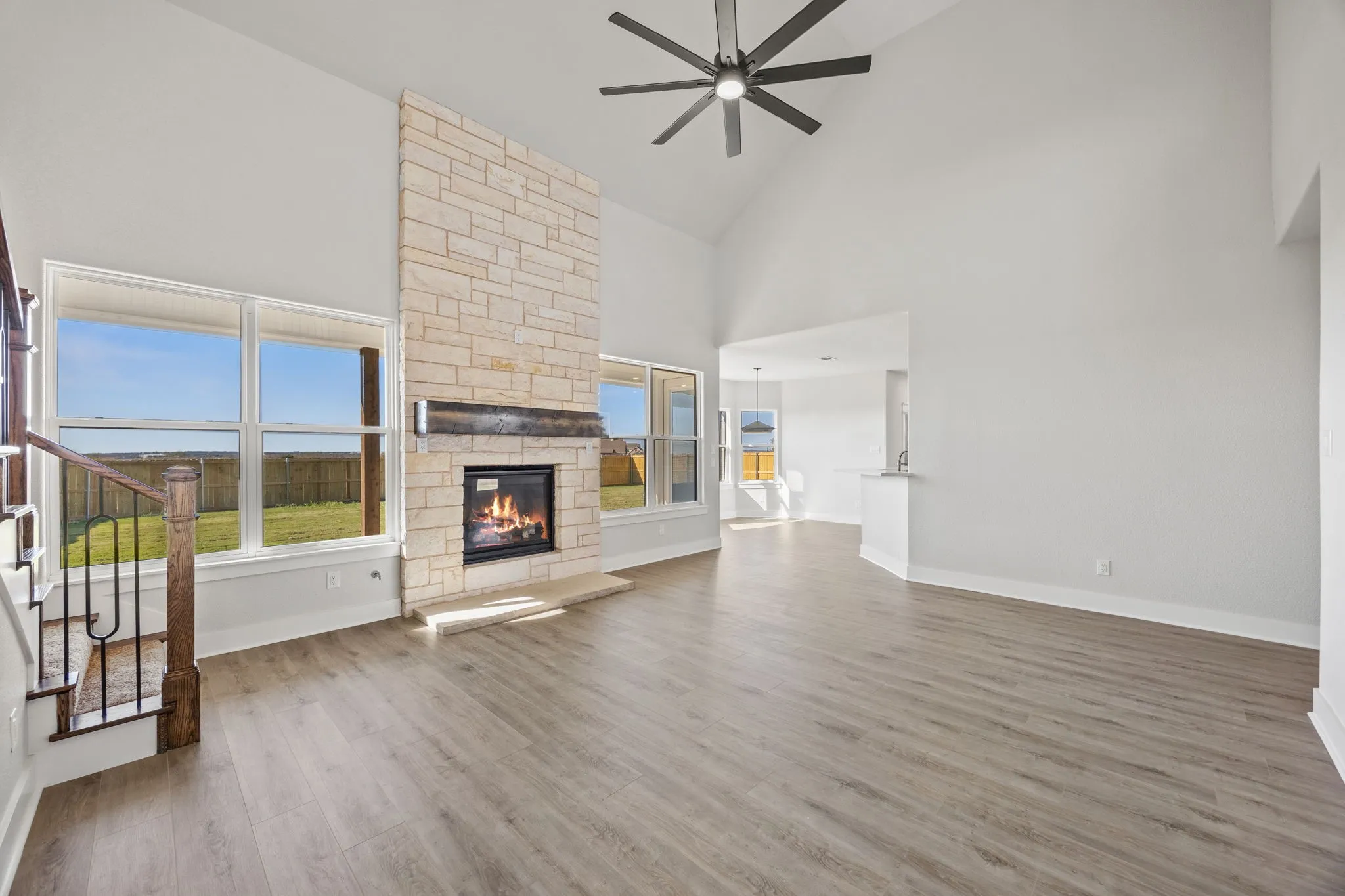 Unfurnished living room featuring high vaulted ceiling, light wood finished floors, a stone fireplace, ceiling fan, and stairs