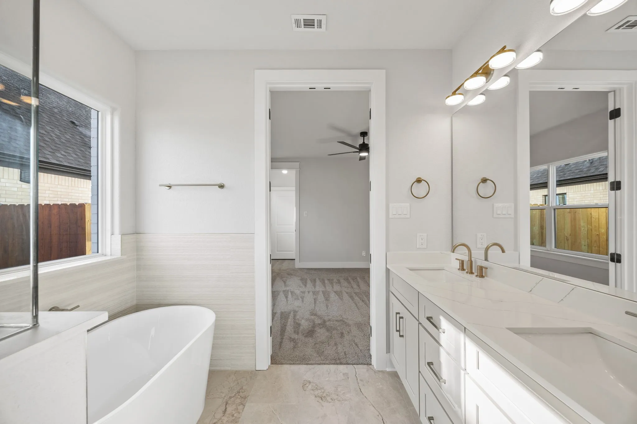 Full bath featuring double vanity, a freestanding bath, a ceiling fan, and light marble finish floors