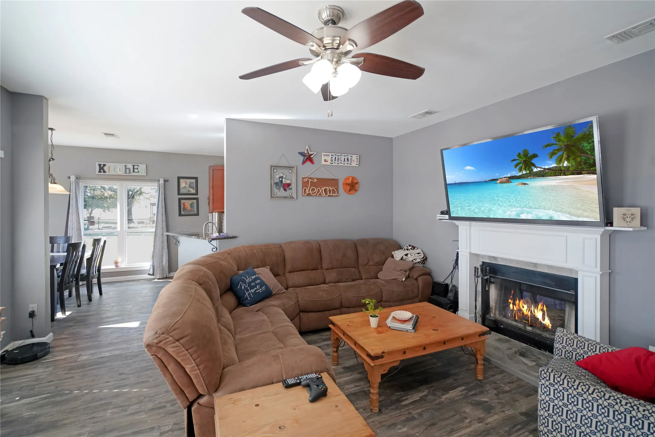Living room featuring dark wood-style flooring, ceiling fan, and a glass covered fireplace