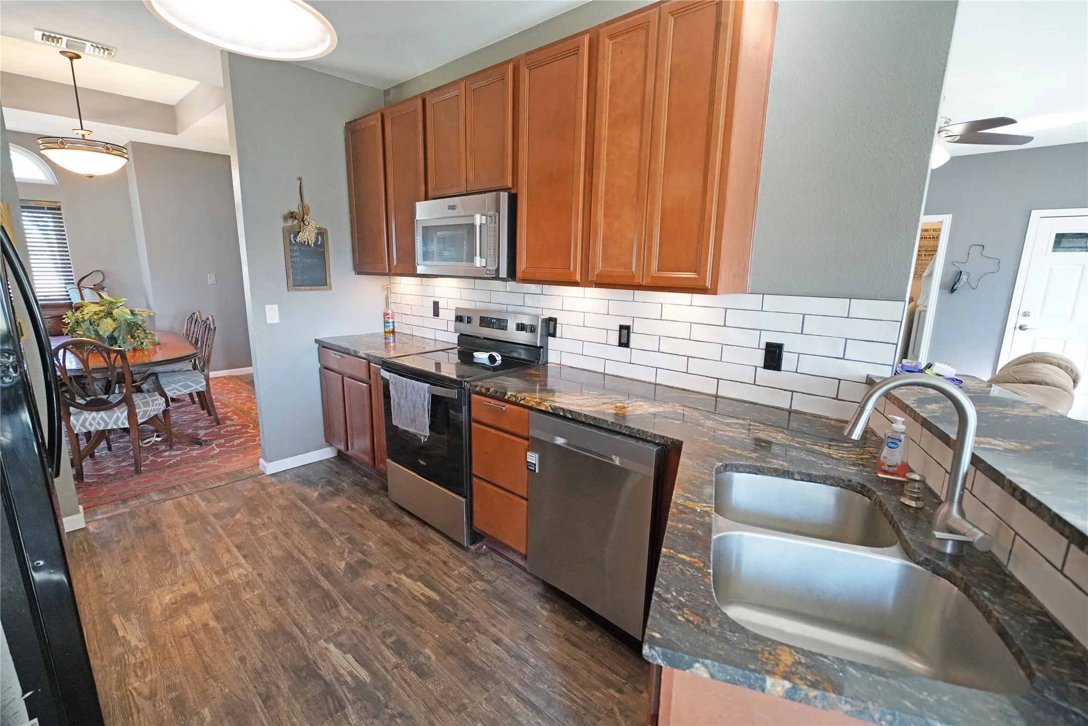 Kitchen featuring stainless steel appliances, brown cabinets, decorative backsplash, and dark wood-type flooring