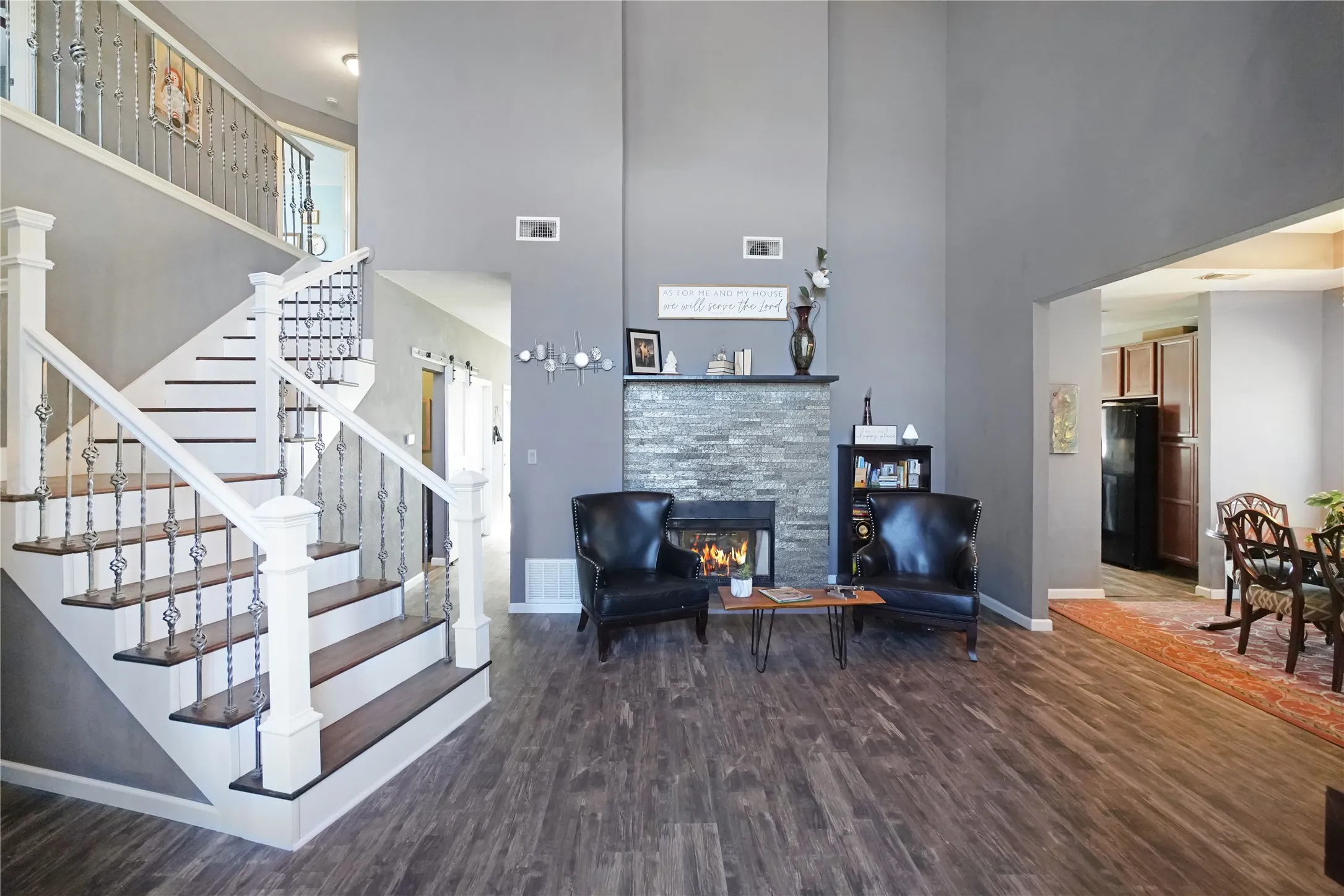 Living area with dark wood-style floors, a high ceiling, a glass covered fireplace, and stairway