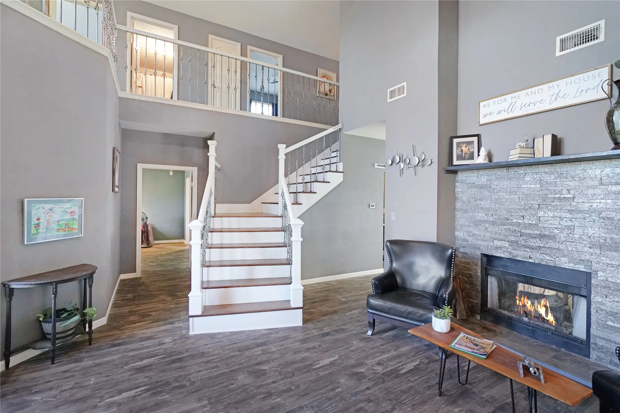 Living area featuring dark wood-style flooring, a high ceiling, stairway, and a stone fireplace