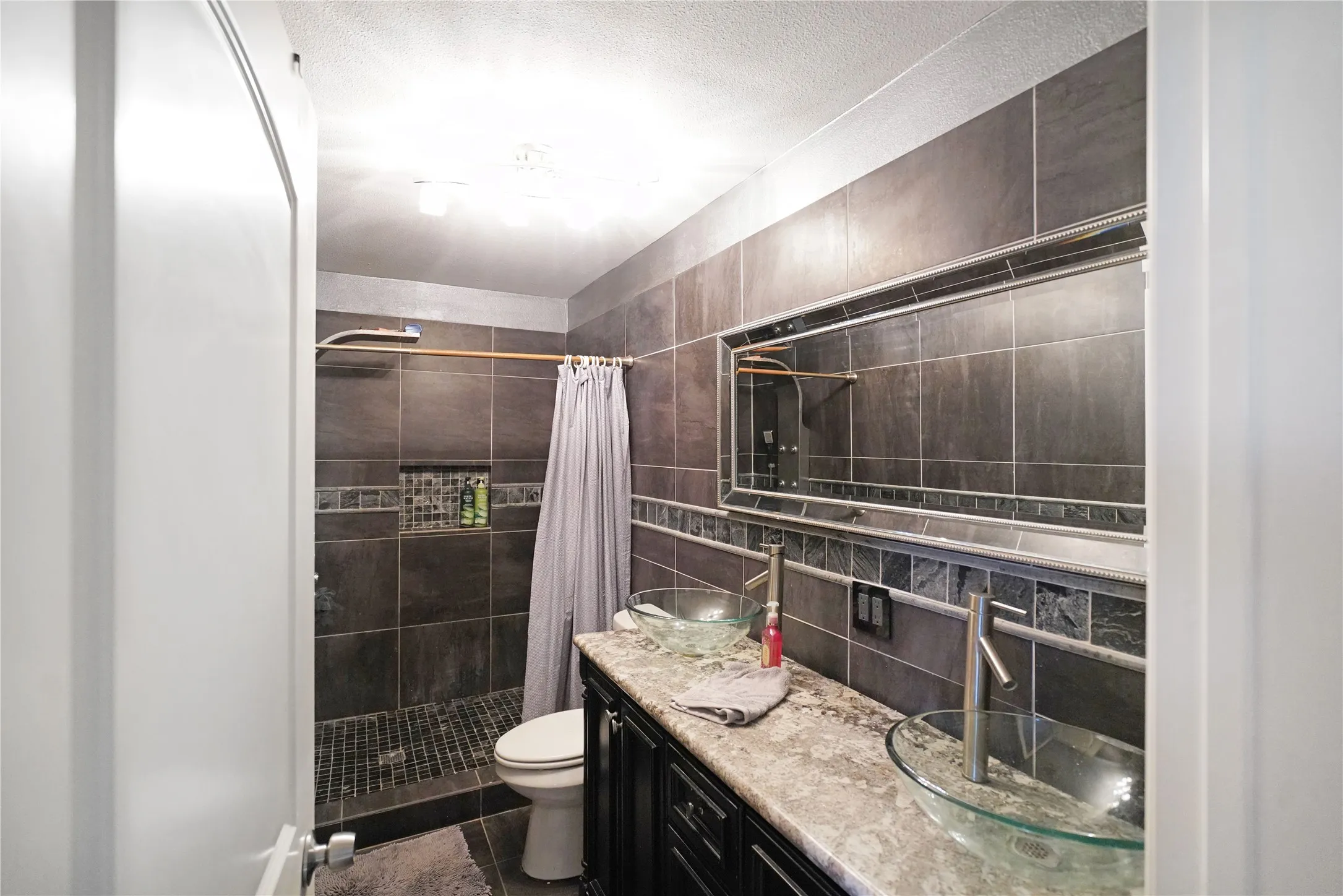 Full bath featuring double vanity, a stall shower, decorative backsplash, a textured ceiling, and tile walls
