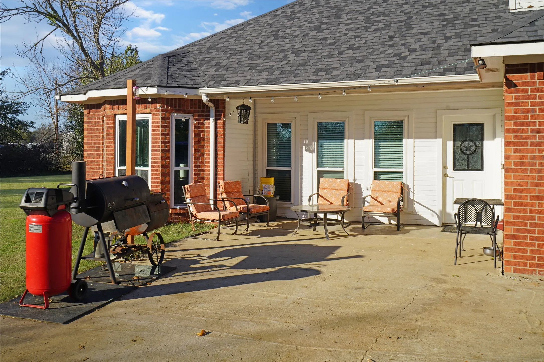 Rear view of house with brick siding, roof with shingles, and a patio area