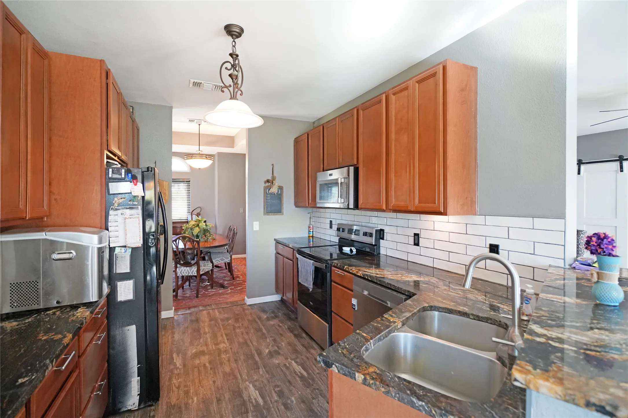 Kitchen featuring appliances with stainless steel finishes, brown cabinets, backsplash, decorative light fixtures, and dark stone counters