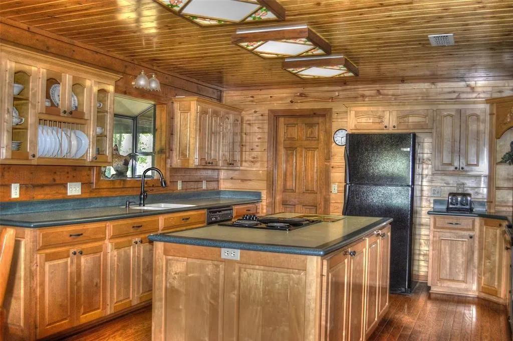 Kitchen with freestanding refrigerator, glass insert cabinets, a kitchen island, wooden ceiling, and dark wood-style flooring
