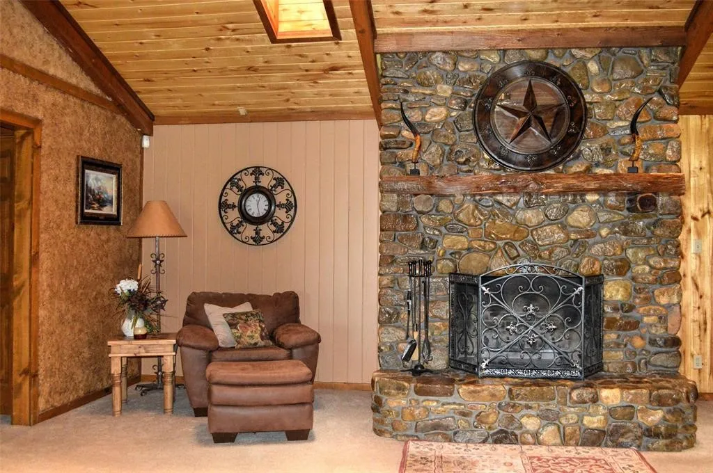 Living area featuring a stone fireplace, lofted ceiling, wooden ceiling, carpet, and wooden walls