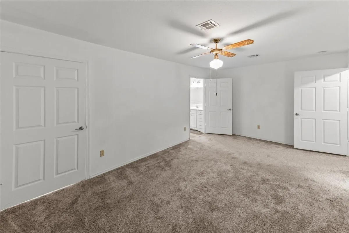 Primary bedroom with carpet flooring, ceiling fan, and ensuite bathroom