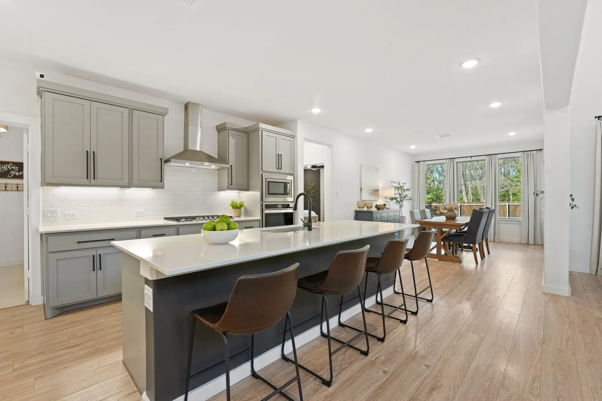 Kitchen with gray cabinetry, a kitchen island with sink, wall chimney range hood, recessed lighting, and light stone counters