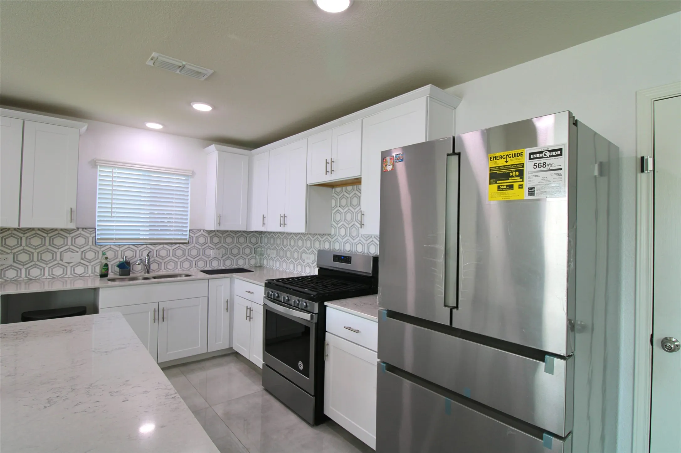 Kitchen featuring appliances with stainless steel finishes, white cabinets, light stone counters, and recessed lighting