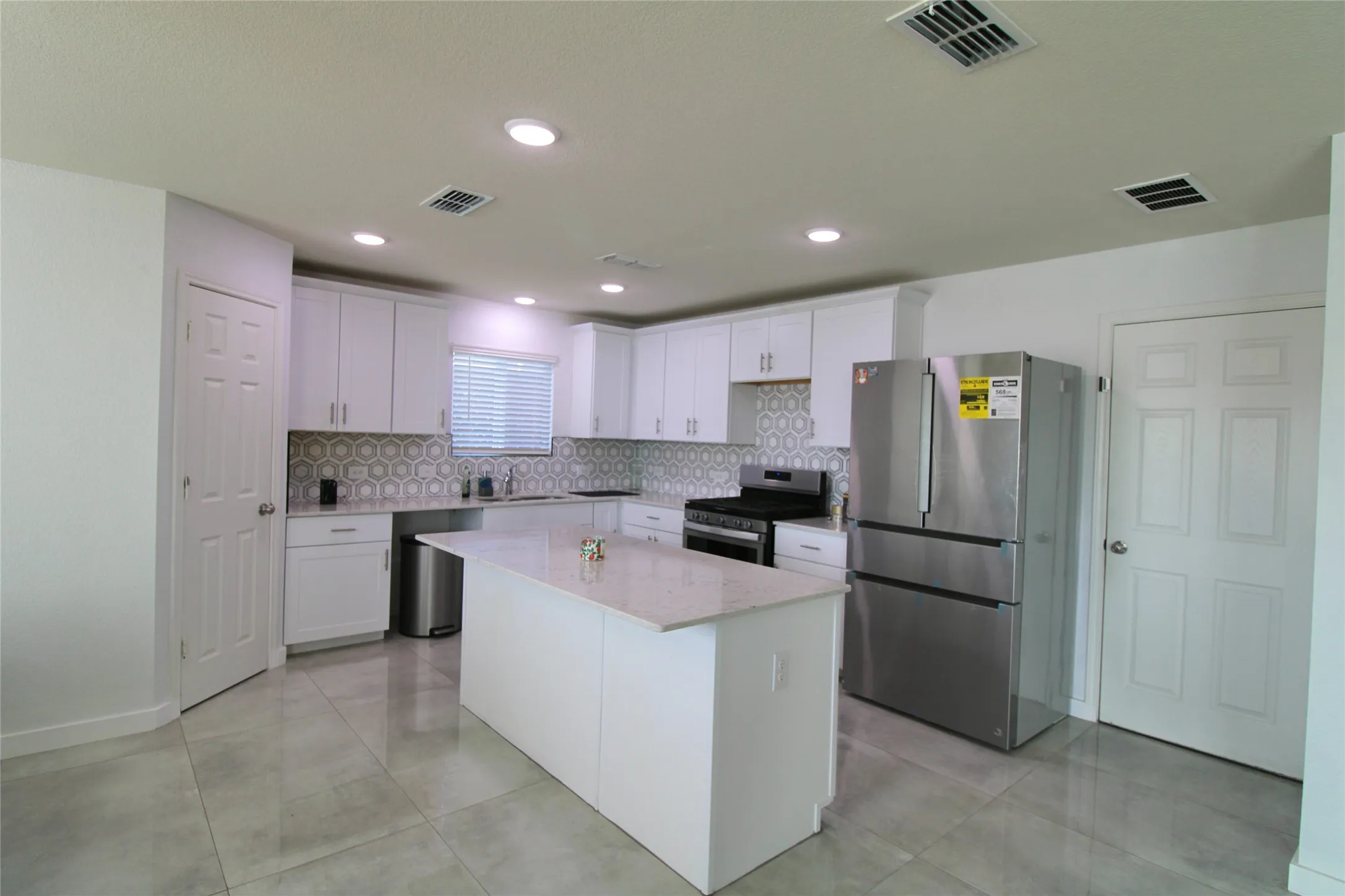 Kitchen with stainless steel appliances, white cabinetry, a center island, light stone countertops, and tasteful backsplash