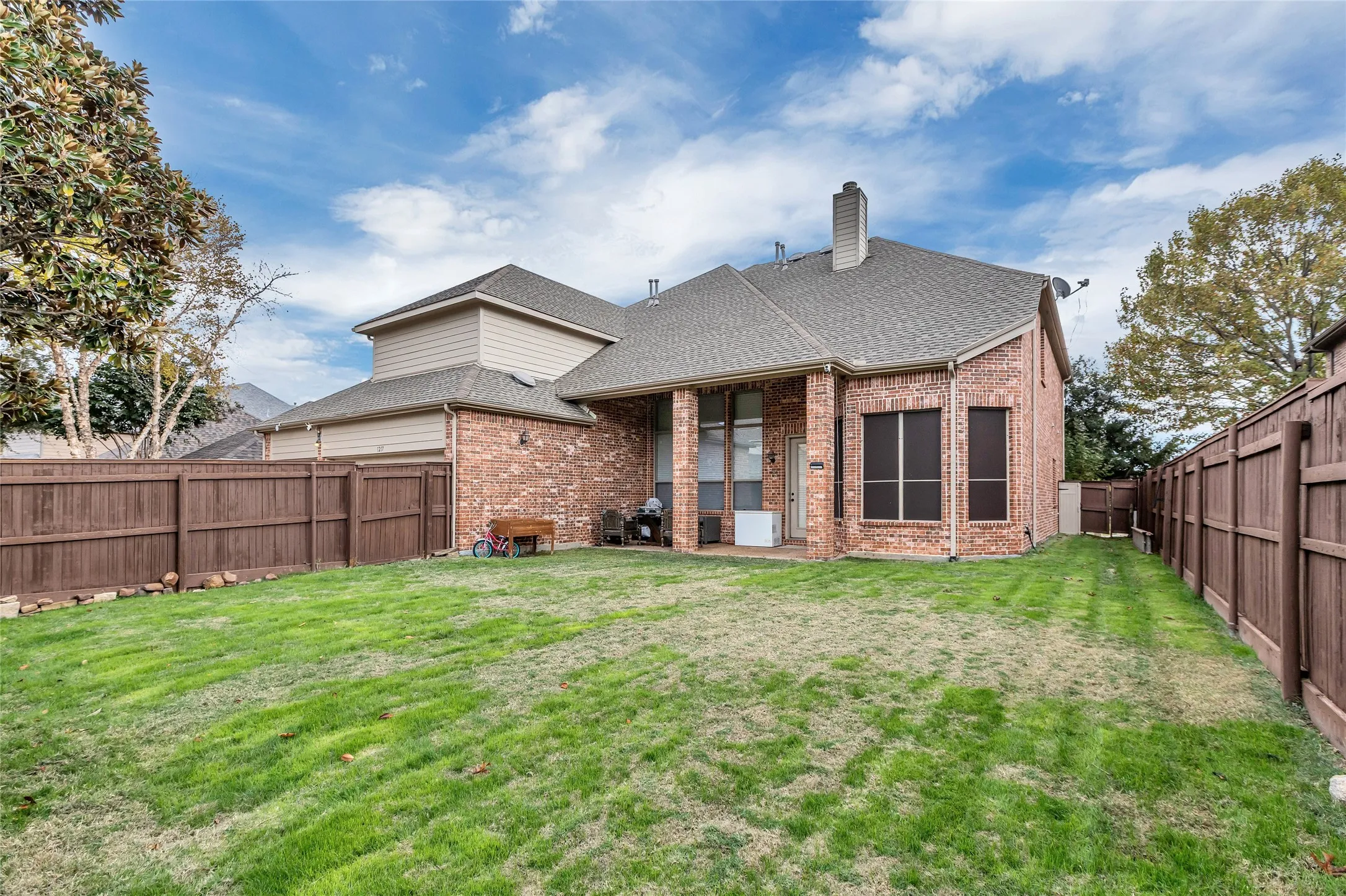 Rear view of house with roof with shingles, a patio, a fenced backyard, brick siding, and a chimney