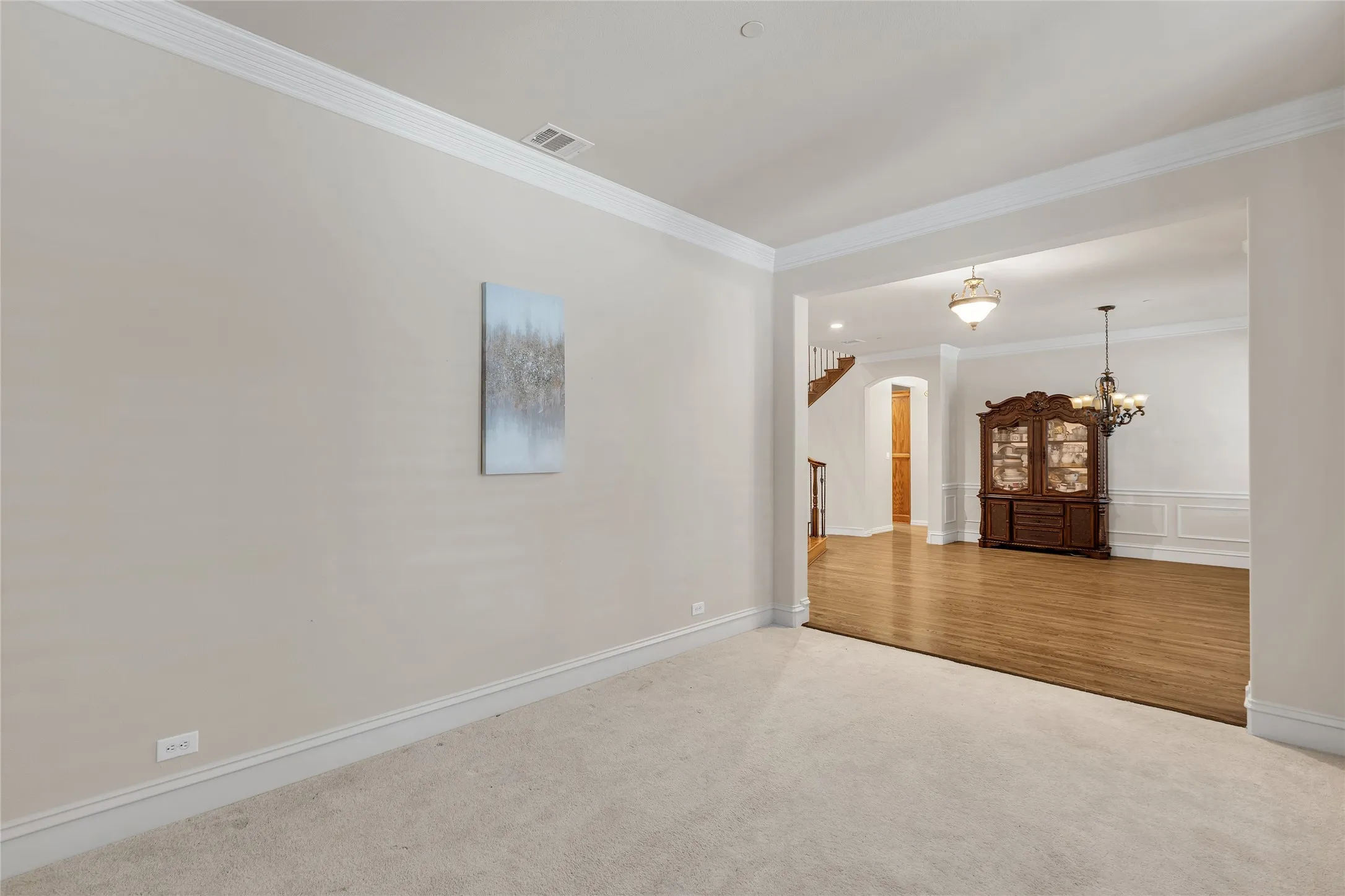 Carpeted spare room with crown molding, a chandelier, and wood finished floors