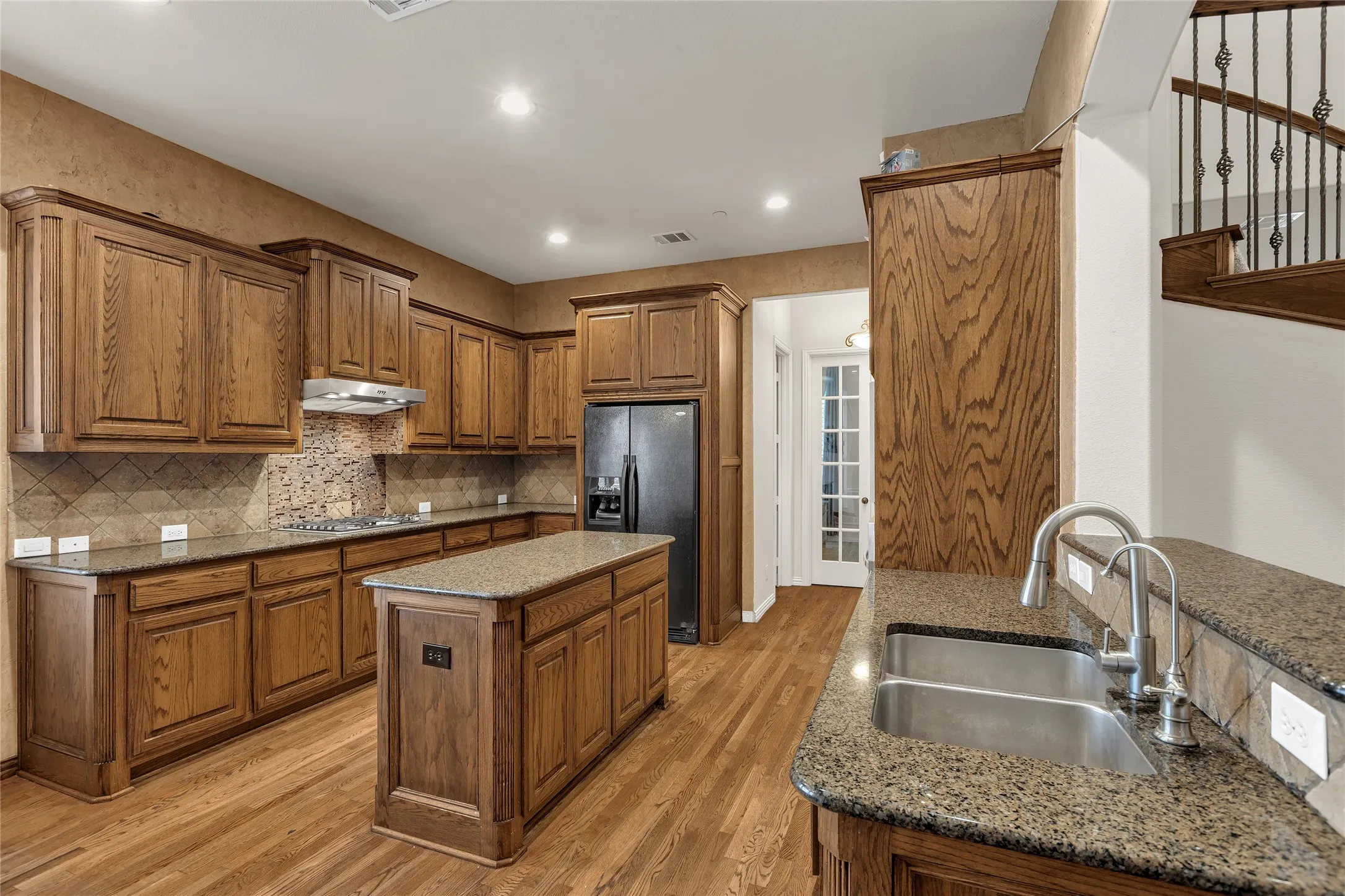 Kitchen featuring brown cabinets, recessed lighting, a center island, black refrigerator with ice dispenser, and light wood-type flooring
