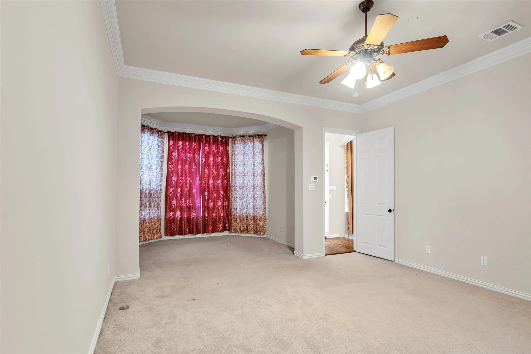 Empty room featuring arched walkways, light carpet, ornamental molding, and ceiling fan