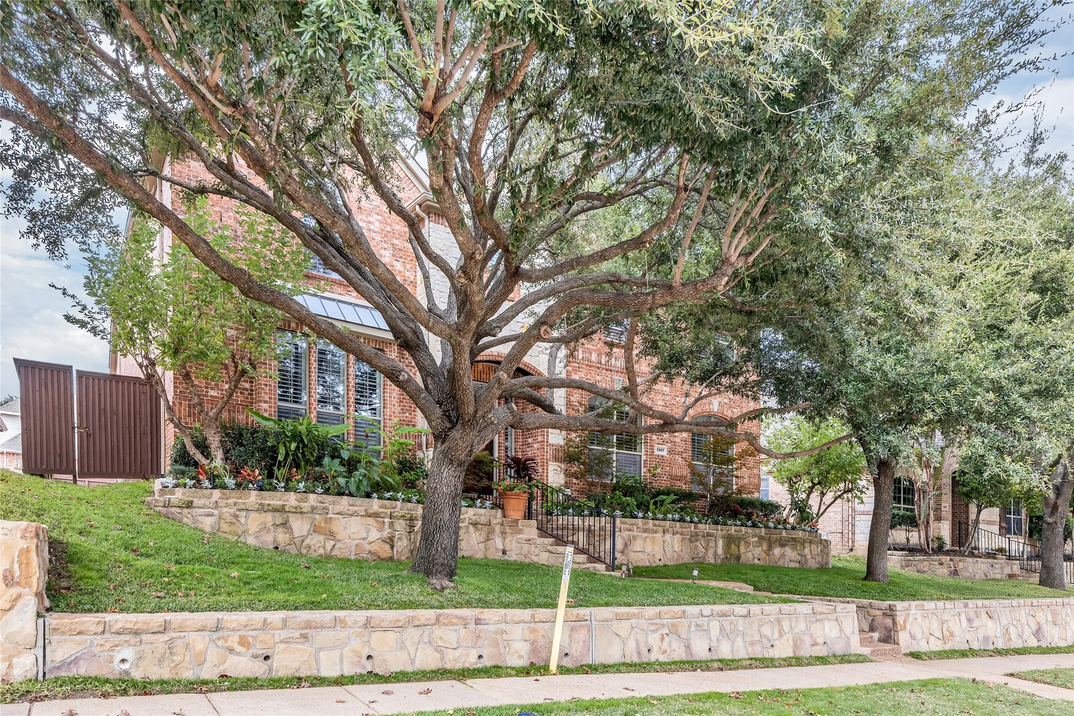 Obstructed view of property featuring a front lawn, brick siding, a standing seam roof, and a metal roof