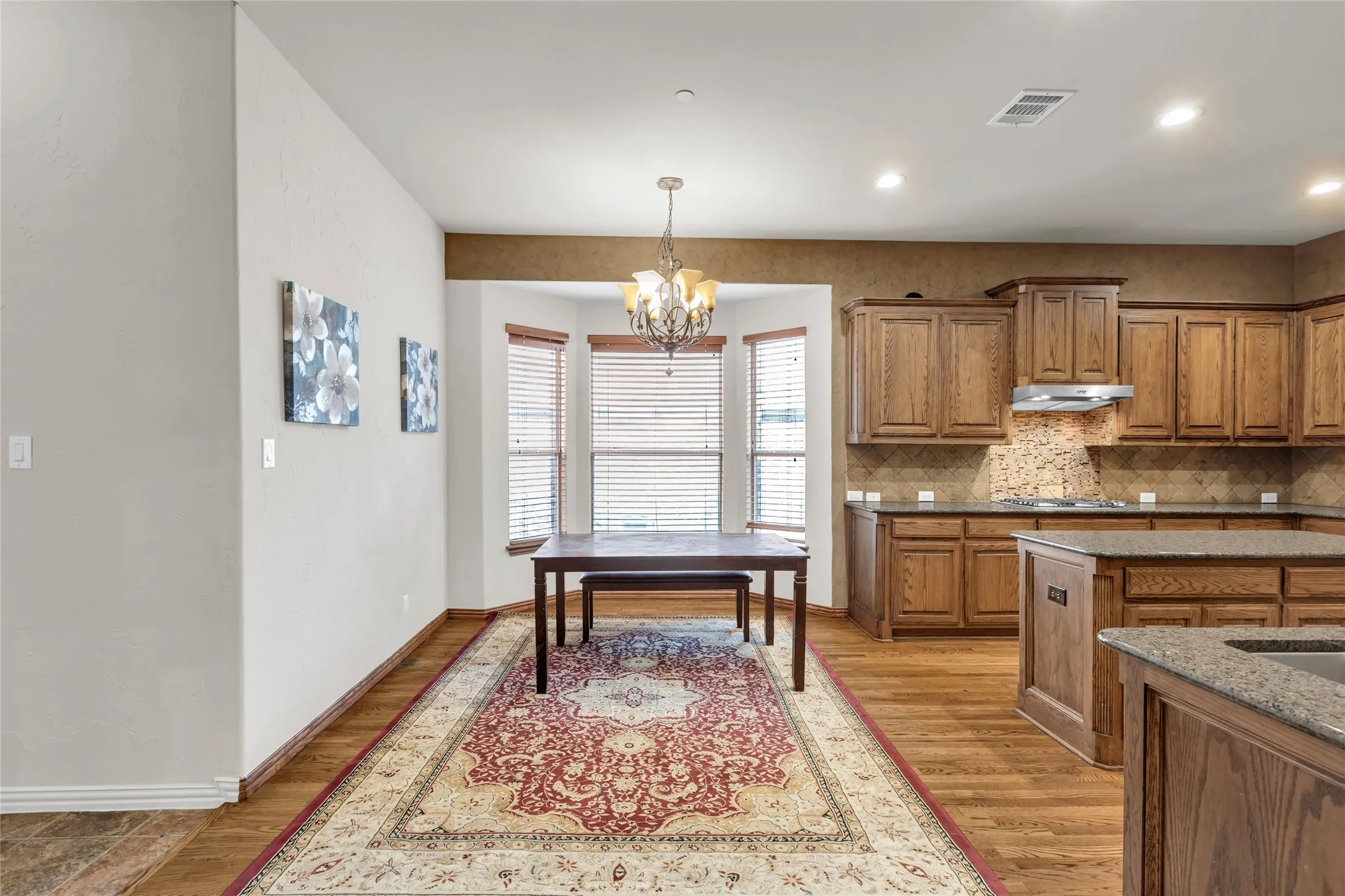 Kitchen with brown cabinetry, backsplash, decorative light fixtures, a chandelier, and light wood finished floors