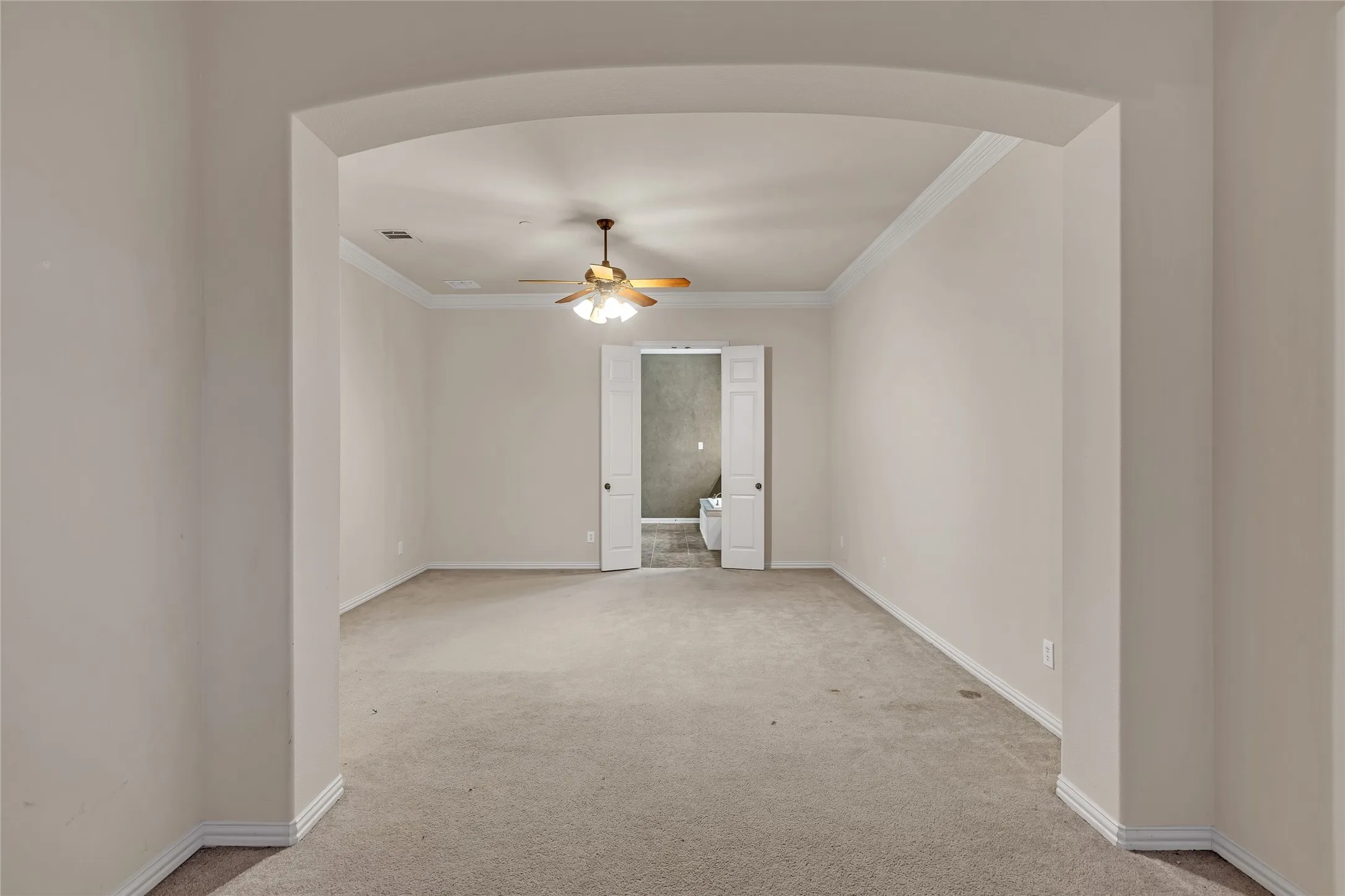 Unfurnished room featuring arched walkways, ornamental molding, light carpet, and a ceiling fan