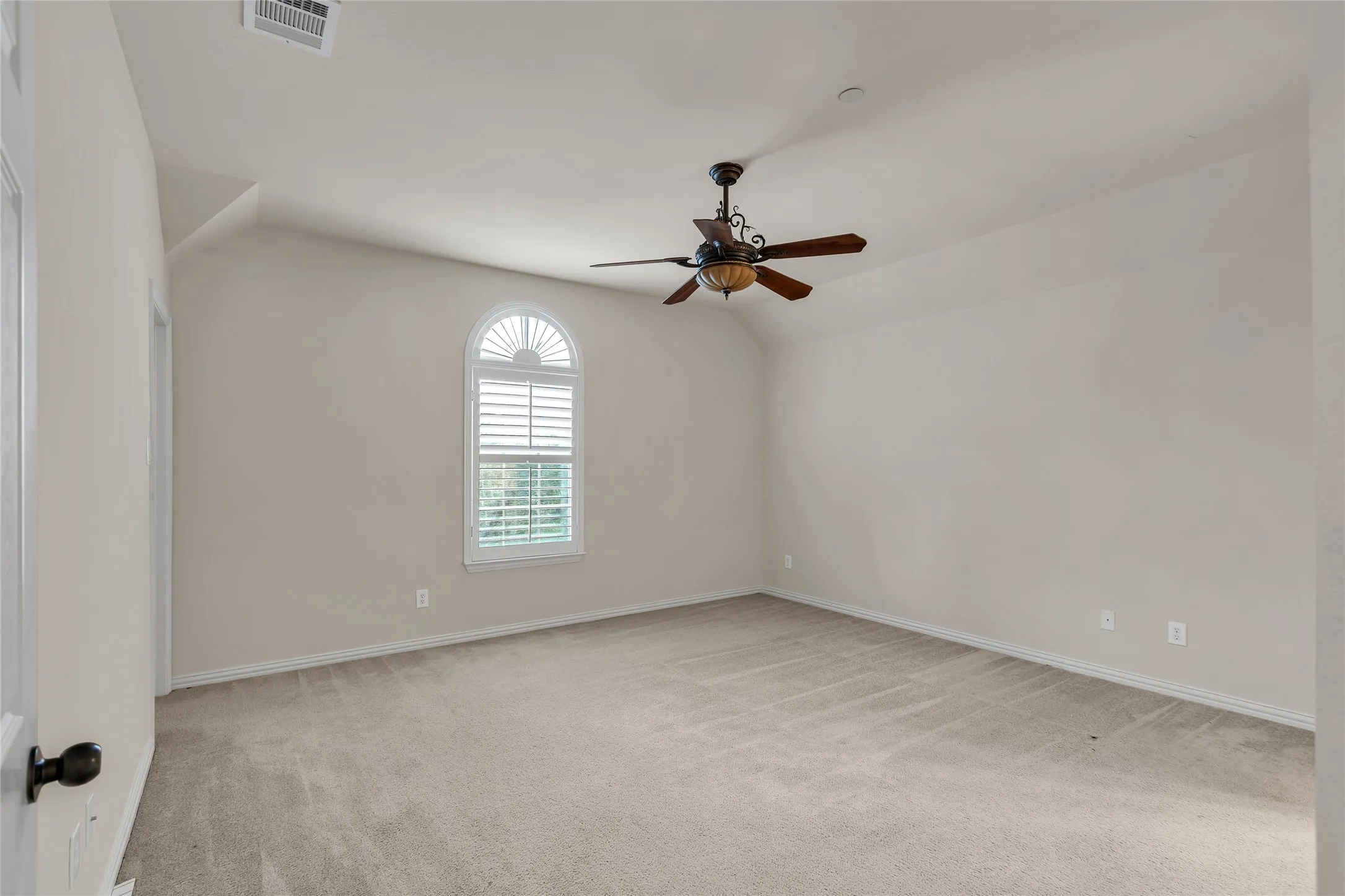 Empty room with light colored carpet, vaulted ceiling, and a ceiling fan