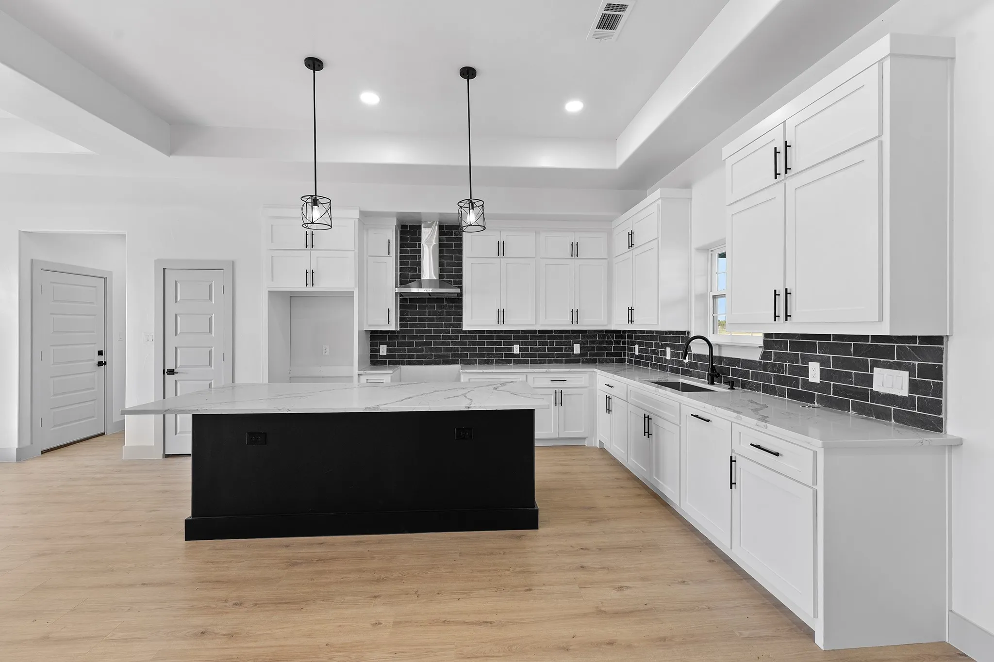 Kitchen with a center island, hanging light fixtures, light stone counters, dark cabinetry, and a tray ceiling