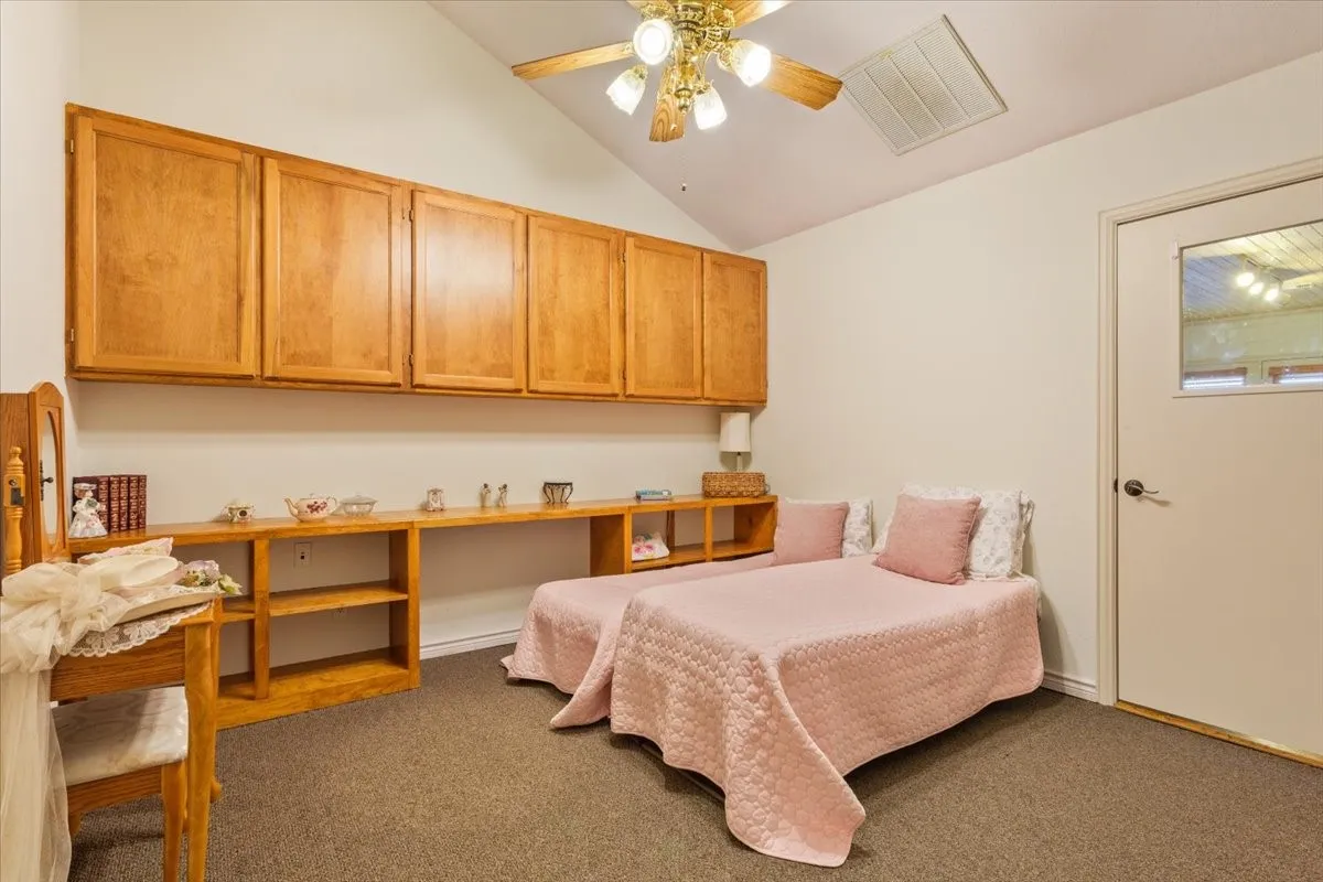 Bedroom with vaulted ceiling, carpet flooring, a ceiling fan, and built in study area