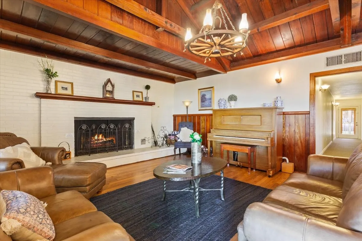 Living room with a wood ceiling with exposed beams, a lit fireplace, wood finished floors, a wainscoted wall, and a chandelier