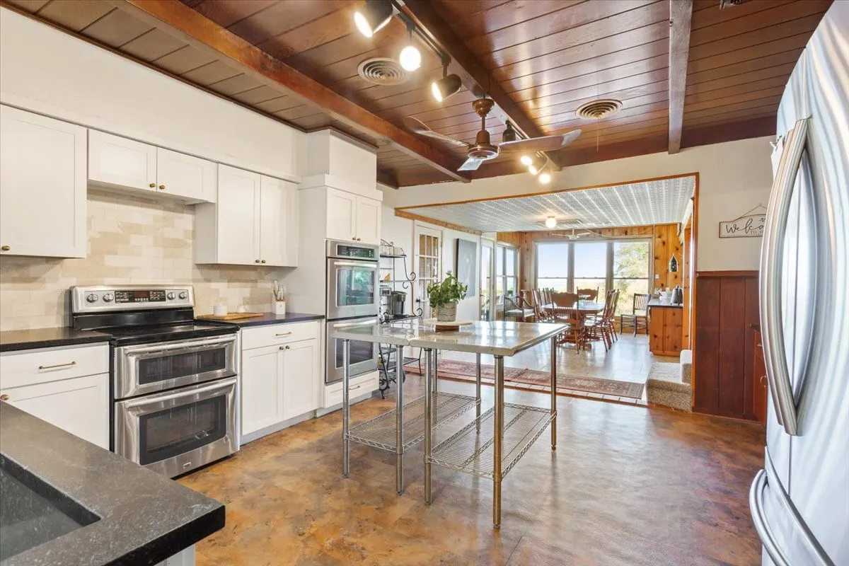 Kitchen with appliances with stainless steel finishes, a wood ceiling with exposed beams, white cabinetry, backsplash, and ceiling fan