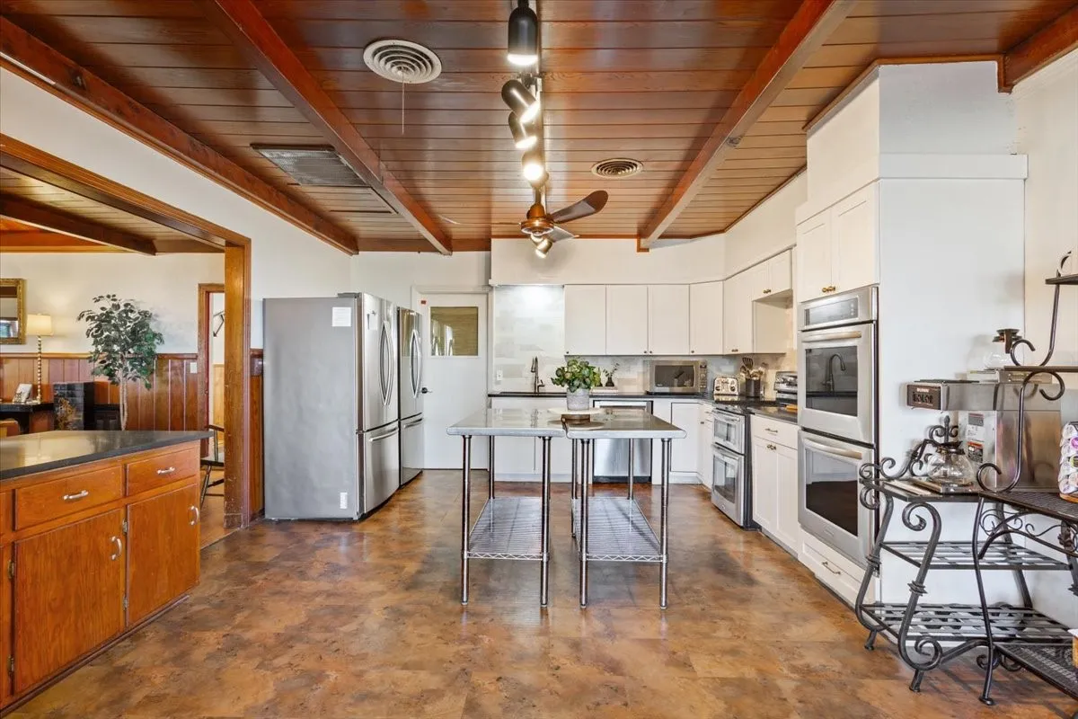 Kitchen with a wooden ceiling with exposed beams, stainless steel appliances, ceiling fan, white cabinetry, and decorative backsplash