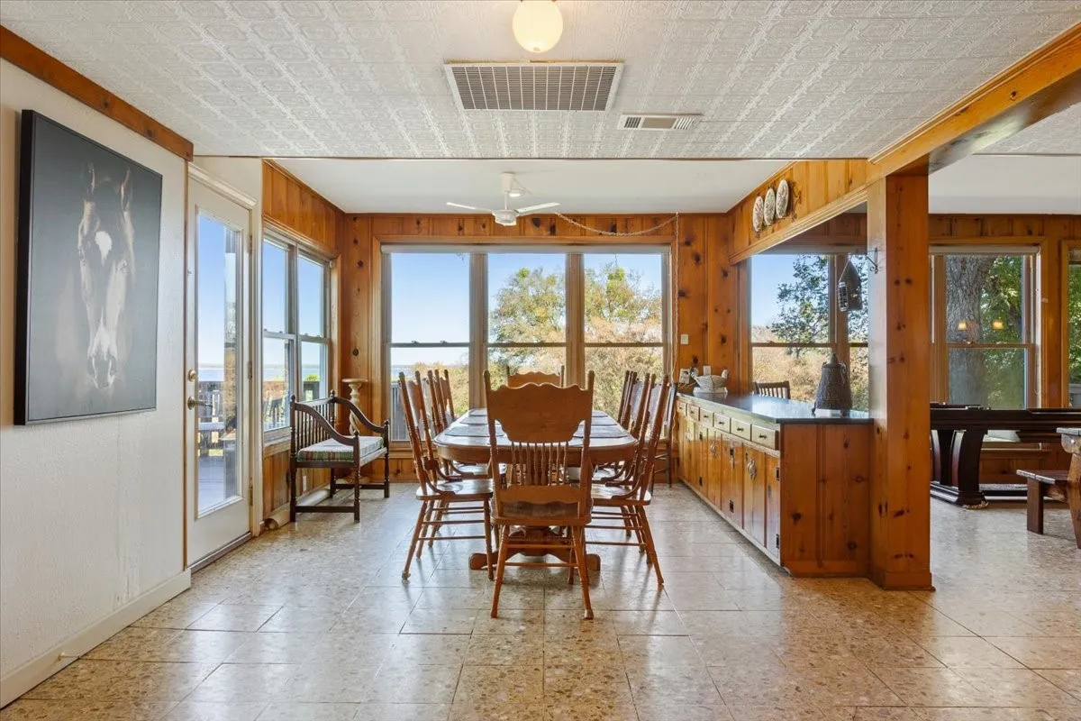 Dining area with healthy amount of natural light, light floors, wood walls, a ceiling fan, and an ornate ceiling
