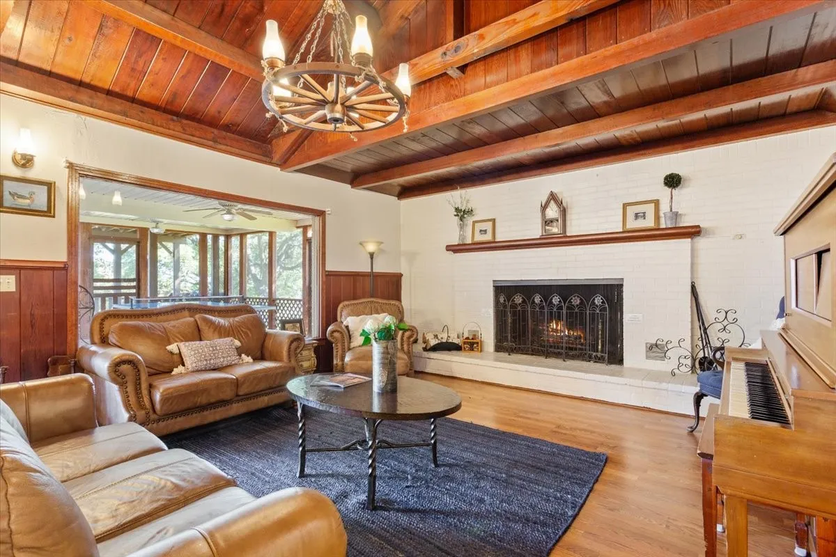 Living area featuring a wood ceiling with exposed beams, a chandelier, wood finished floors, a wainscoted wall, and a brick fireplace