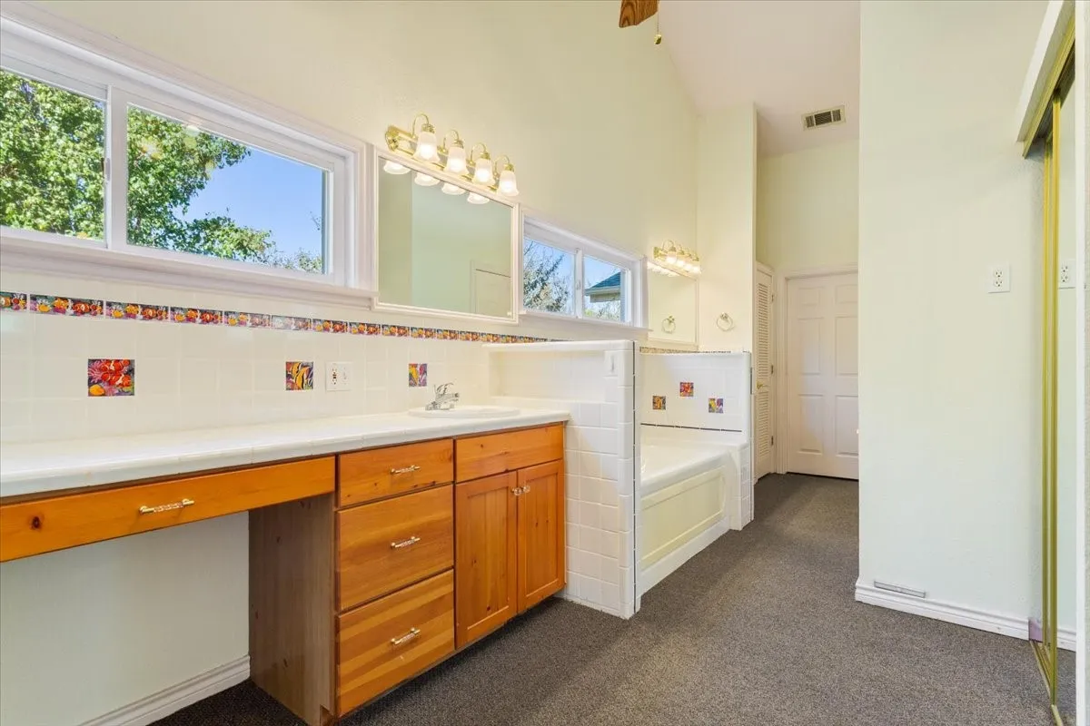Bathroom featuring vanity, dark colored carpet, a bath, decorative backsplash, and ceiling fan