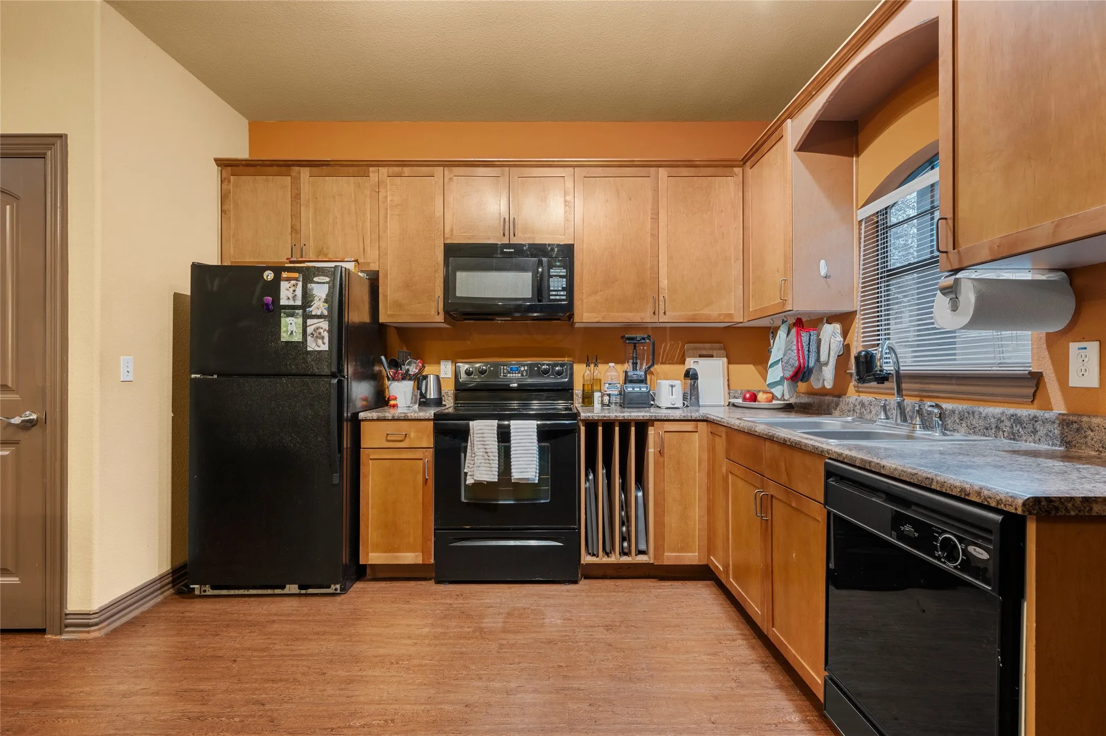 Kitchen featuring black appliances, light wood-type flooring, brown cabinets, and light countertops
