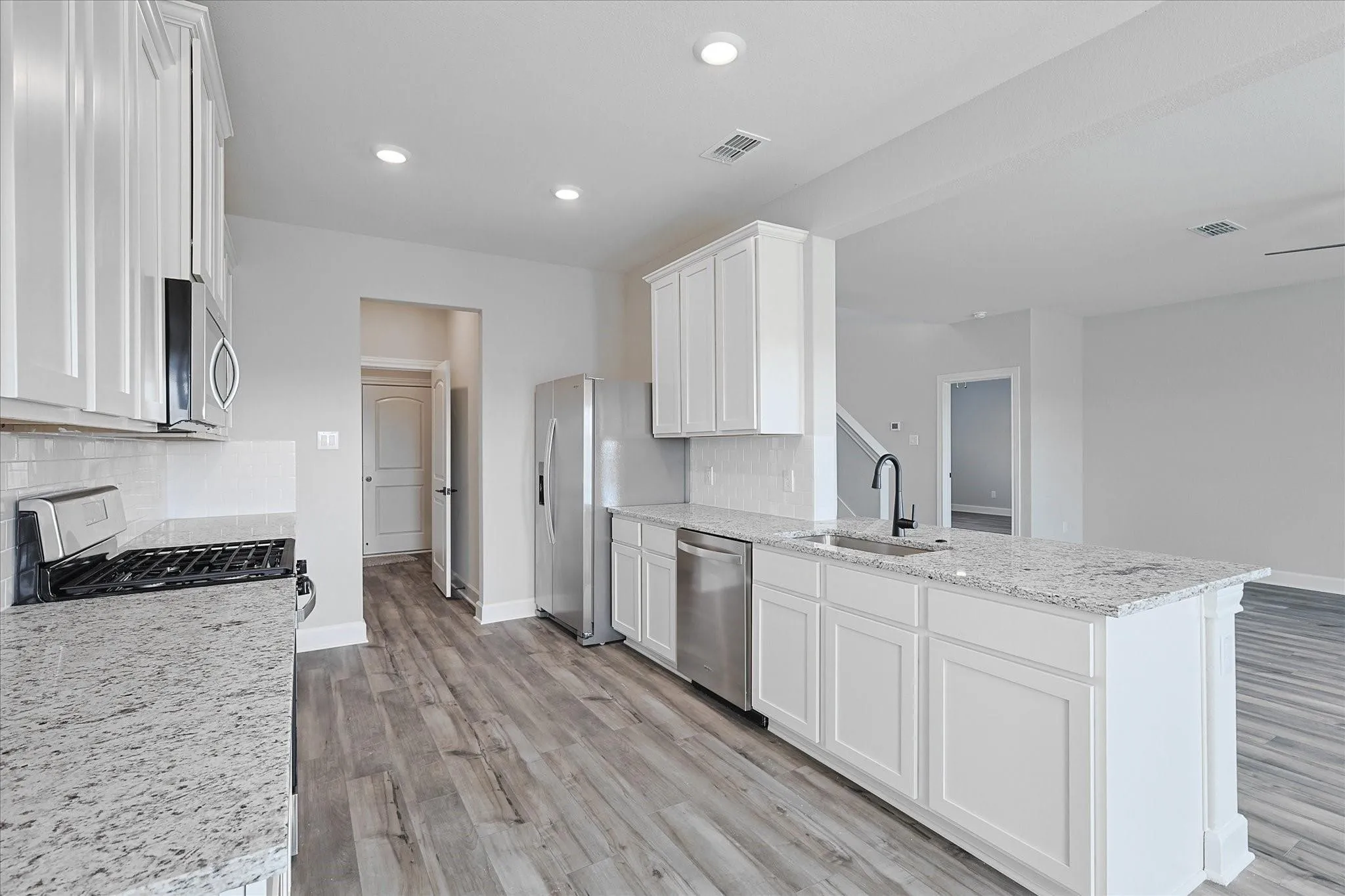 Kitchen featuring white cabinets, light stone countertops, light wood-type flooring, backsplash, and recessed lighting
