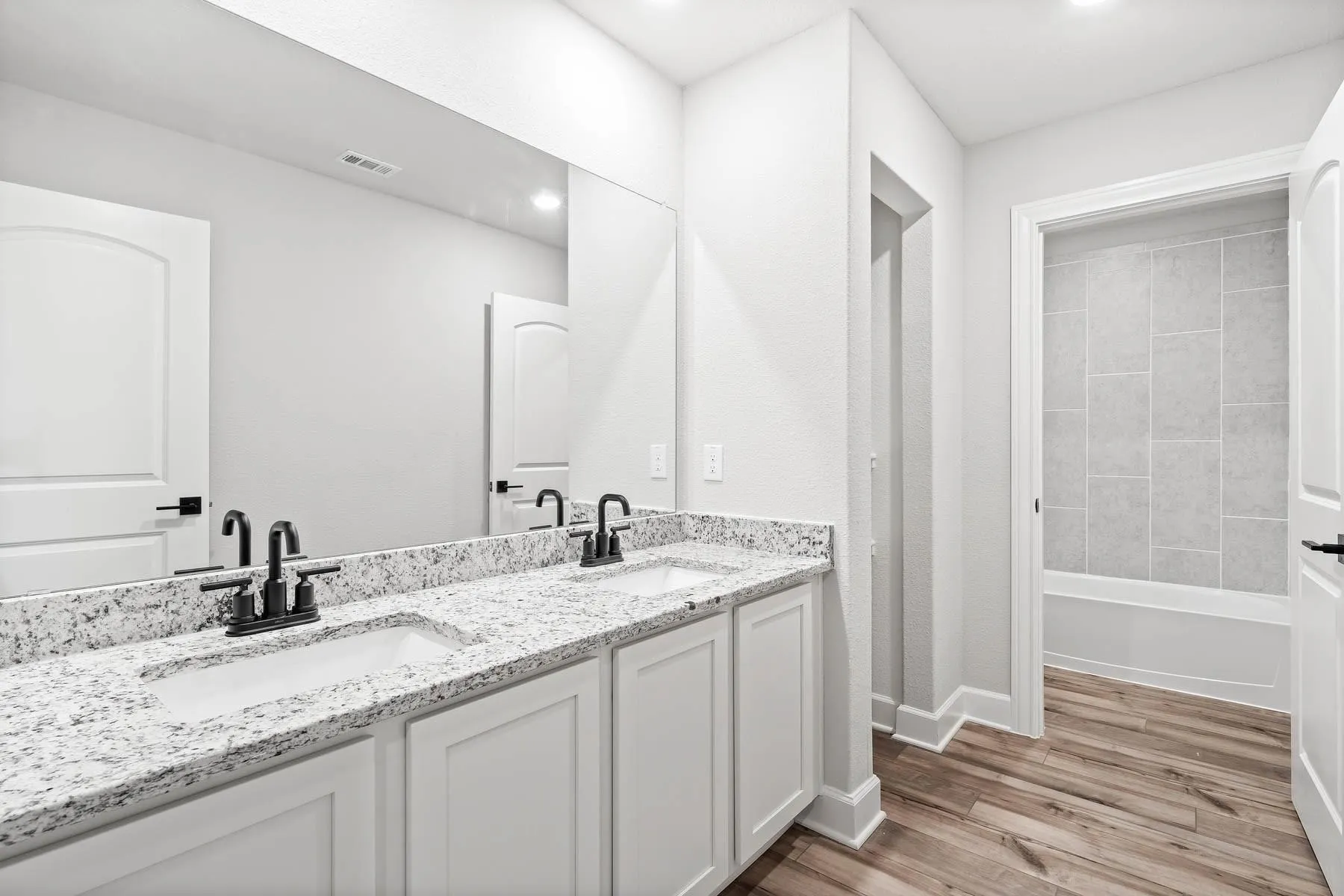 Full bathroom featuring double vanity, light wood-style floors, and a tub to relax in