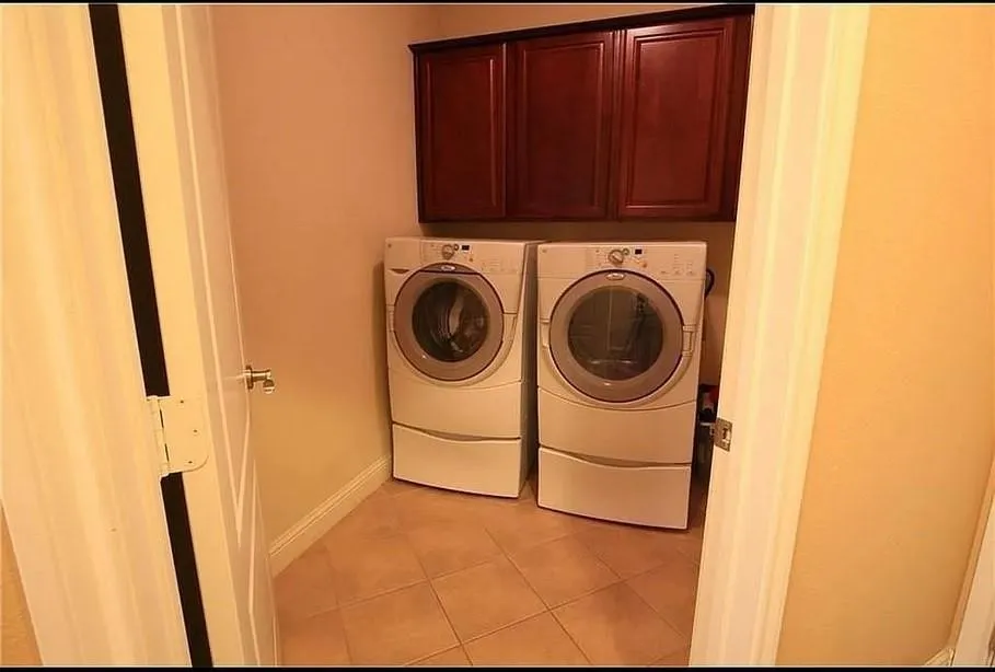 Laundry room featuring light tile patterned floors, washing machine and dryer, and cabinet space
