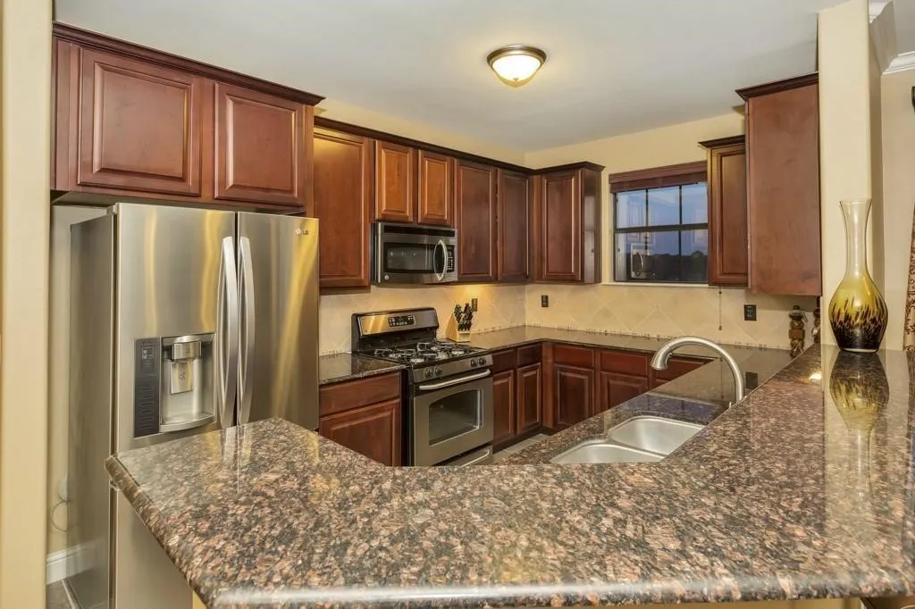Kitchen featuring stainless steel appliances, dark stone countertops, backsplash, and a peninsula