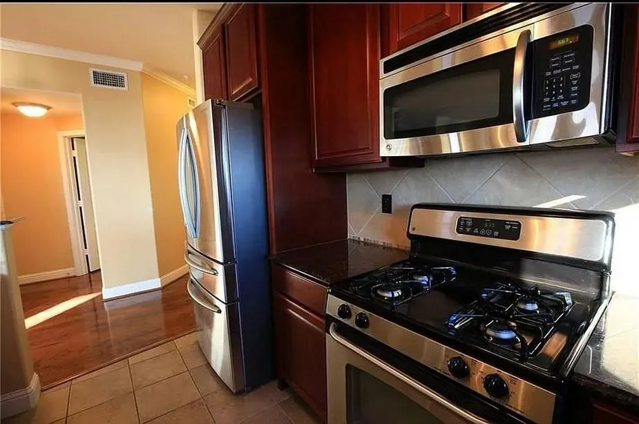 Kitchen featuring appliances with stainless steel finishes, crown molding, dark stone countertops, dark tile patterned floors, and dark brown cabinets