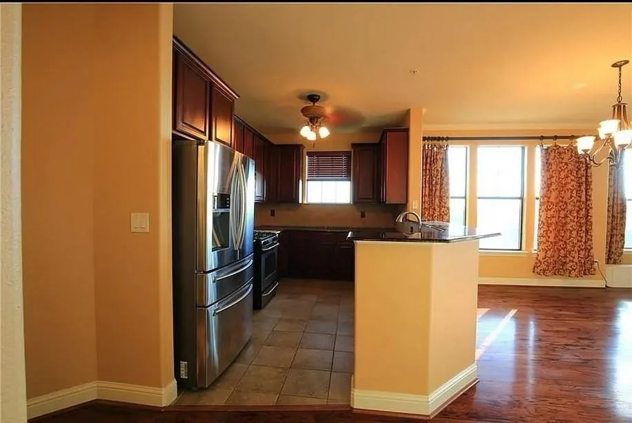 Kitchen with stainless steel fridge, a peninsula, dark wood-type flooring, a chandelier, and range with gas cooktop