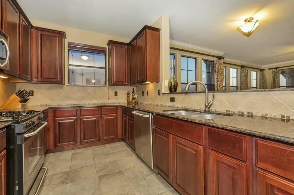 Kitchen with reddish brown cabinets, tasteful backsplash, appliances with stainless steel finishes, dark stone countertops, and crown molding
