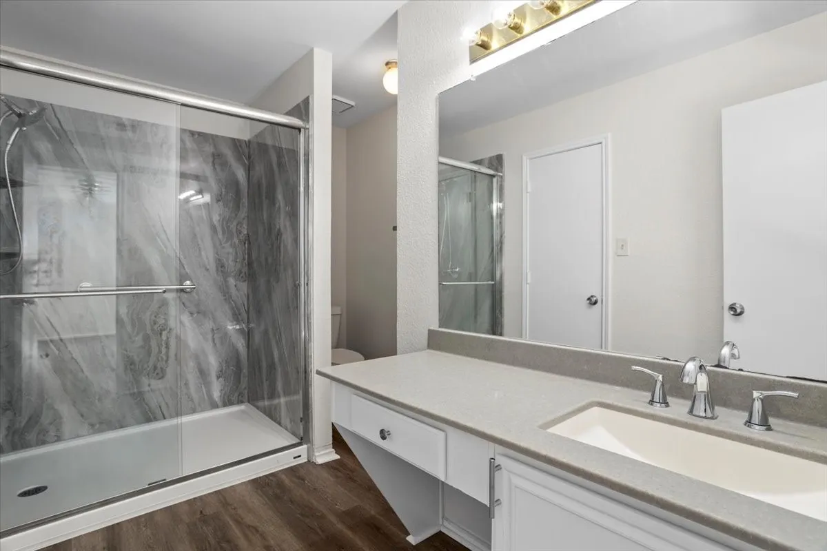 Bathroom featuring vanity, a marble finish shower, and dark wood-type flooring