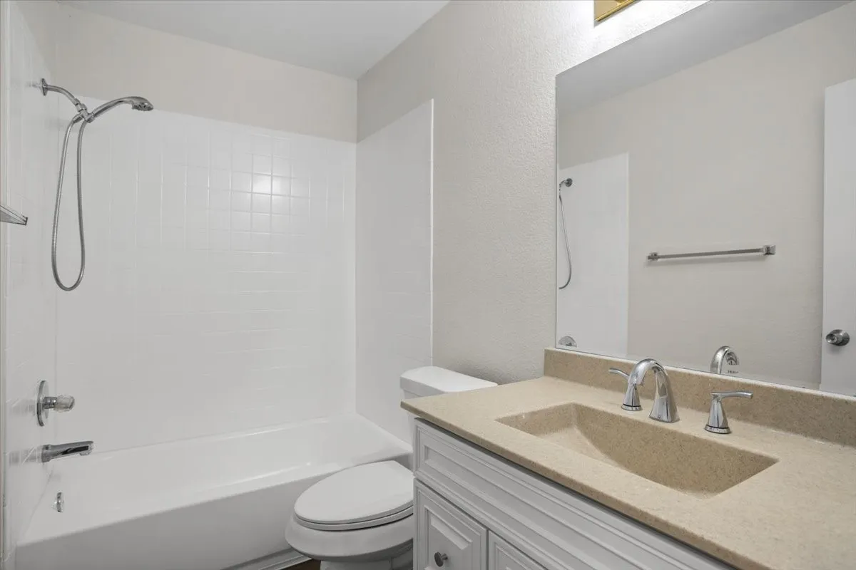 Bathroom with washtub / shower combination, vanity, and a textured wall