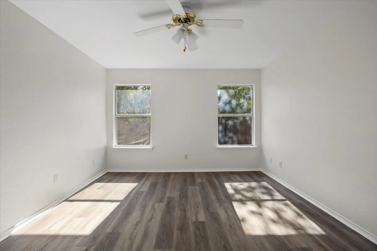 Empty room with healthy amount of natural light, dark wood-style flooring, and ceiling fan