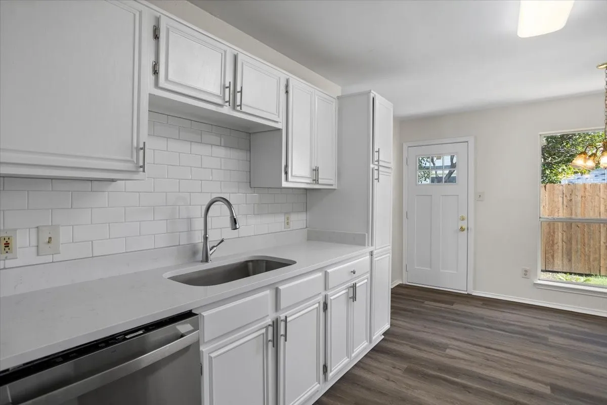 Kitchen with dishwasher, light stone countertops, dark wood-type flooring, white cabinetry, and tasteful backsplash