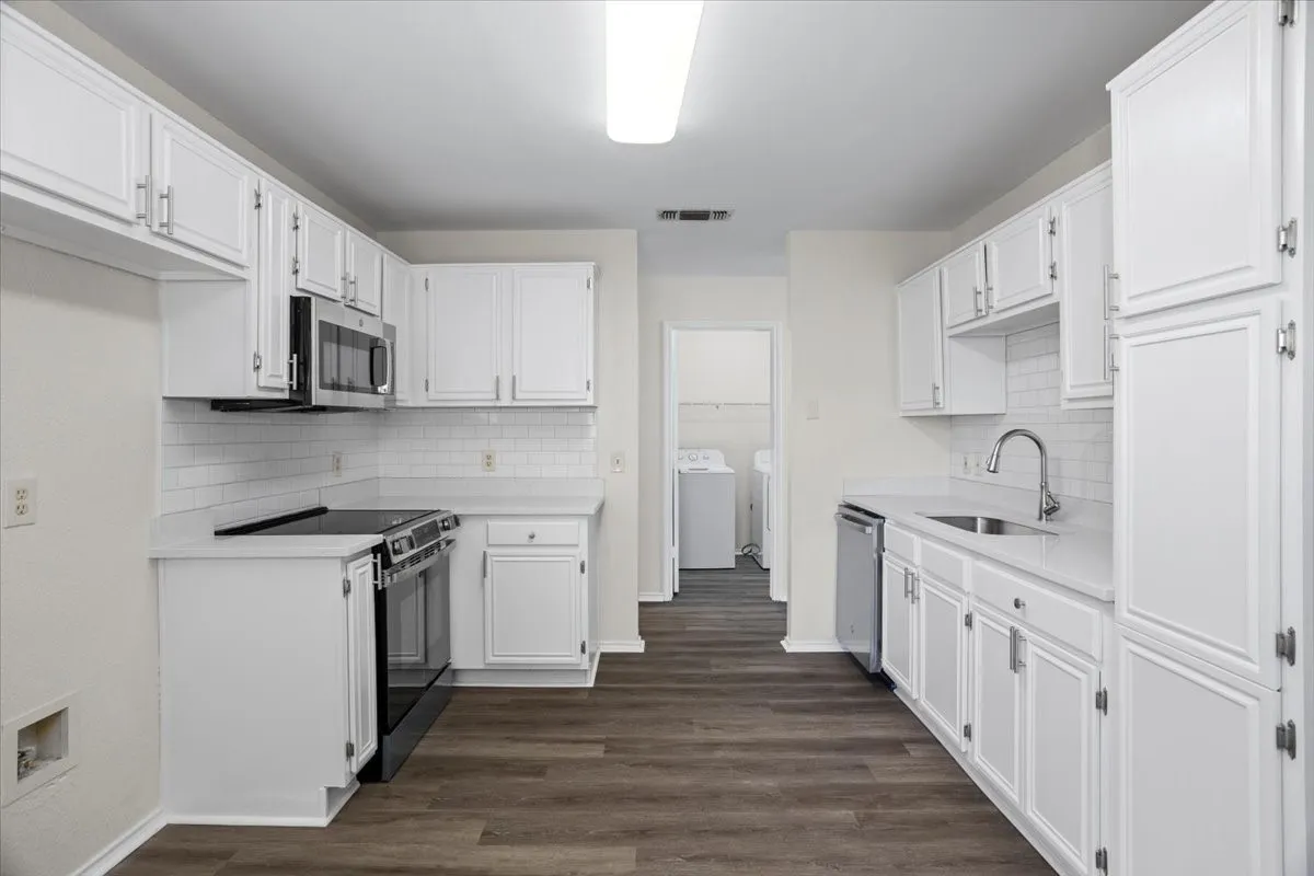 Kitchen with appliances with stainless steel finishes, white cabinetry, dark wood-style flooring, and backsplash