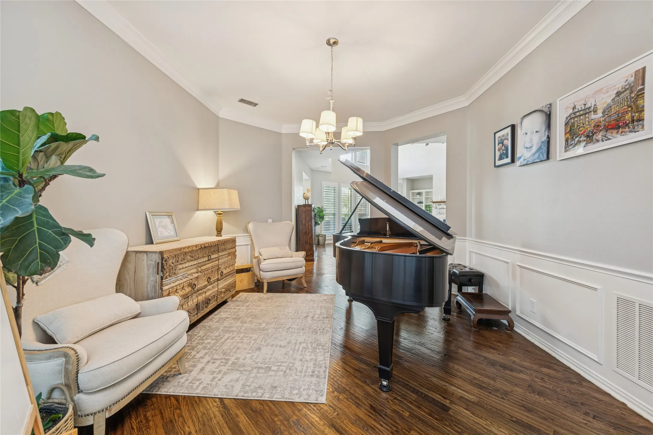 Living area with dark wood-style floors, crown molding, a chandelier, a decorative wall, and wainscoting