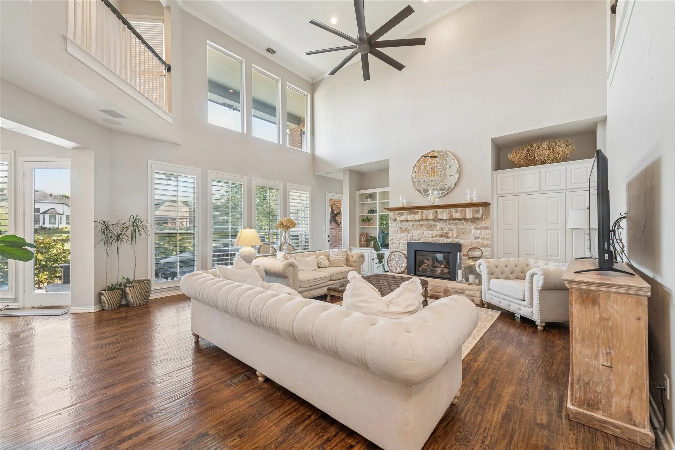 Living room featuring a stone fireplace, built in shelves, dark wood-style flooring, a towering ceiling, and ornamental molding